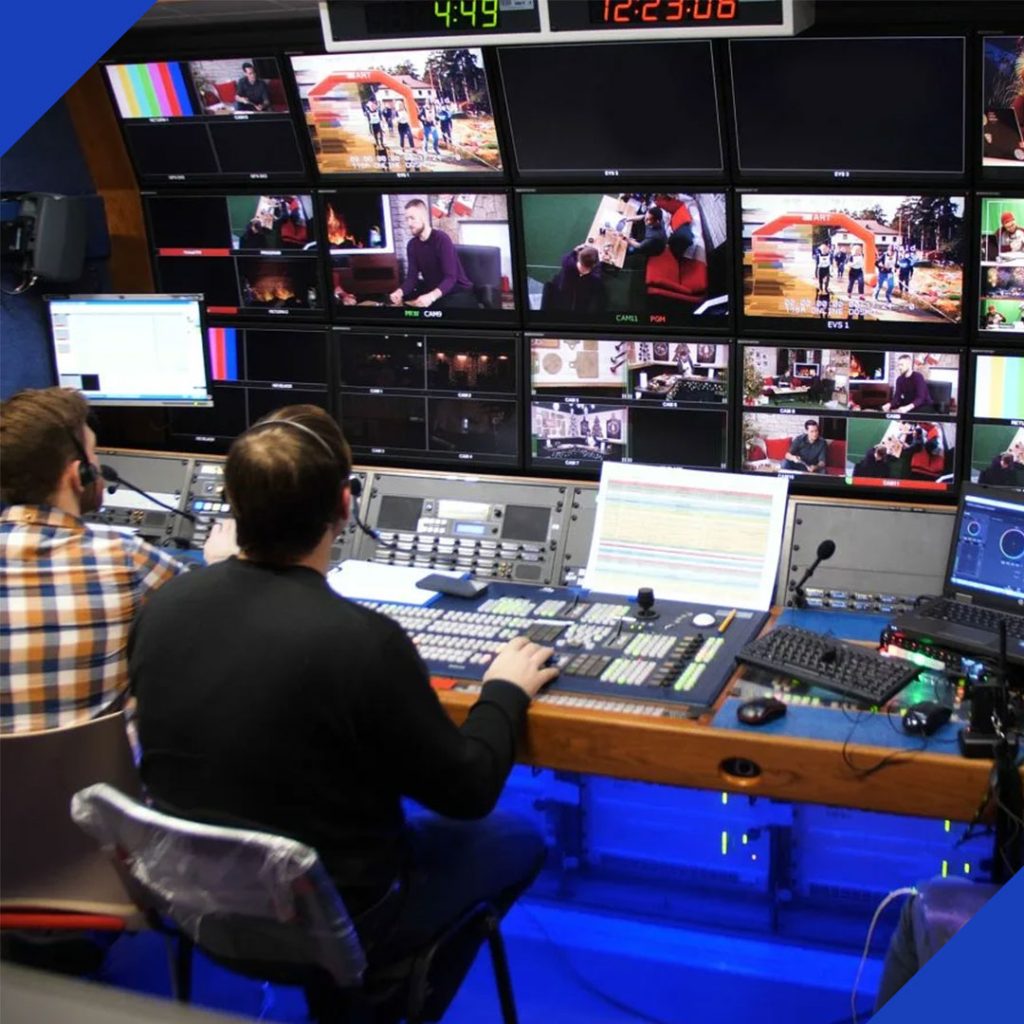 Two technicians working at a professional broadcast control desk with multiple video monitors, representing the expert digital broadcasting services from JR Digital Media.